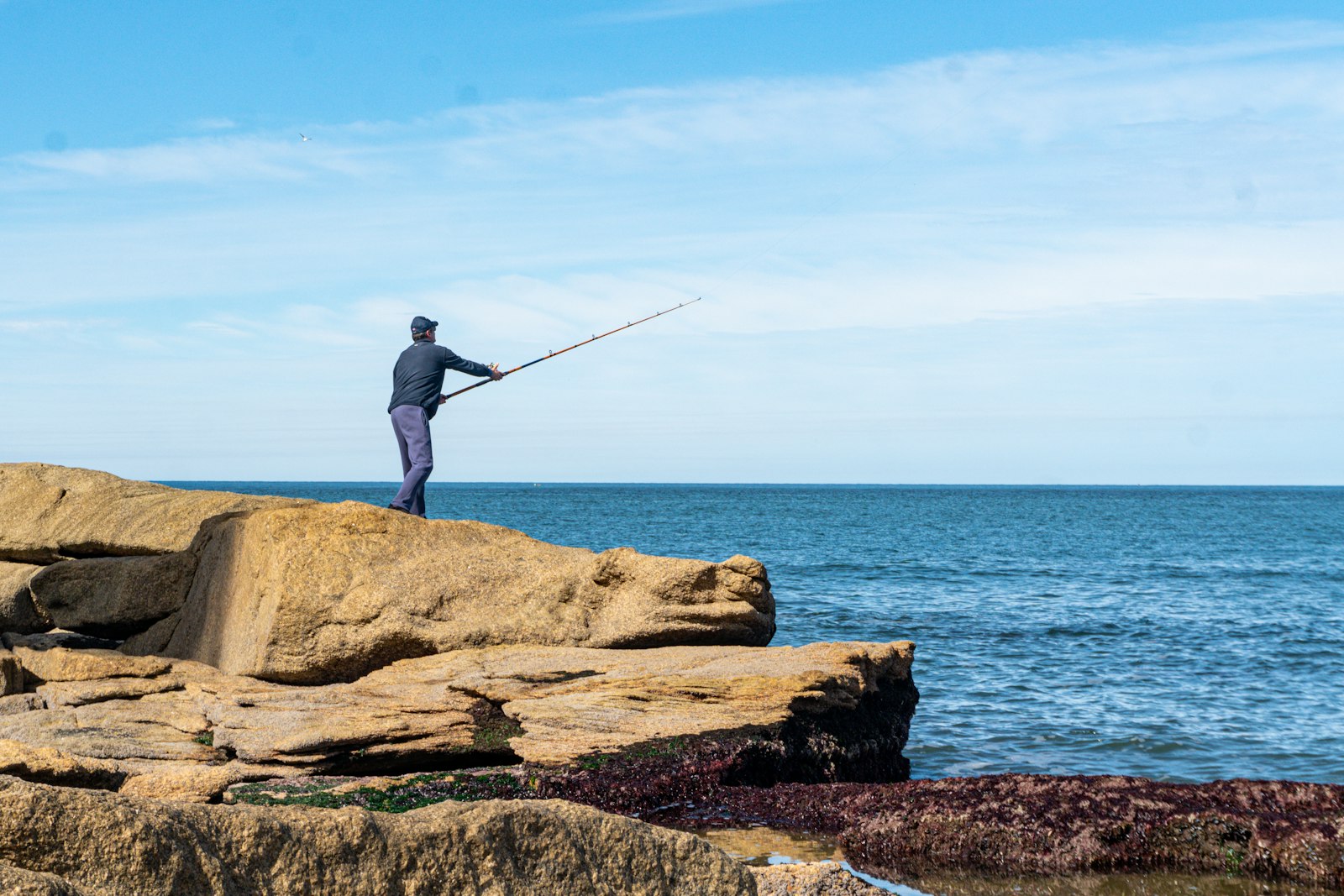 Pescatore a spinning sugli scogli in riva al mare