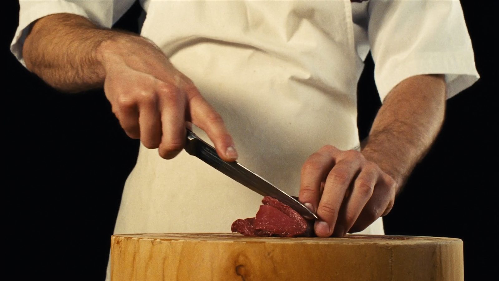 Le mani del macellaio che rifila un taglio di carne sul tagliere